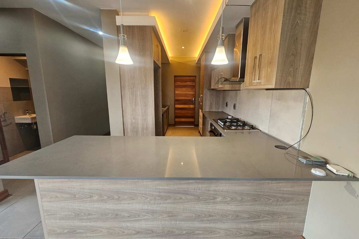 Modern kitchen featuring wood-grain cabinetry, stone countertops, a breakfast bar, integrated gas hob, and recessed ceiling lighting.