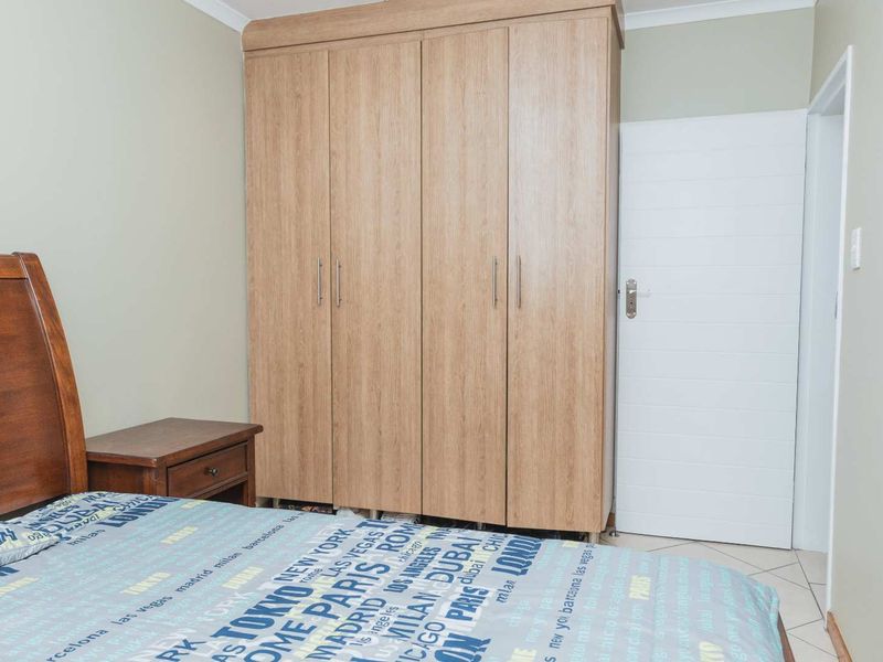 A bedroom featuring light wood-finish built-in wardrobes, tiled flooring, and a white internal door.