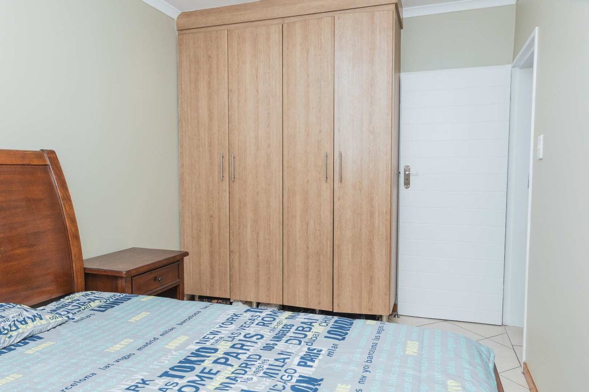 A bedroom featuring light wood-finish built-in wardrobes, tiled flooring, and a white internal door.