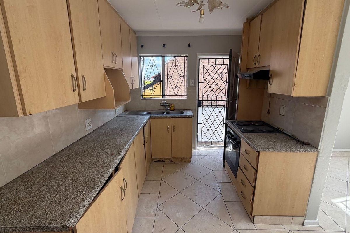A functional kitchen featuring laminate cabinetry, granite-look countertops, a built-in stove with extractor, and direct access to an exterior security gate.