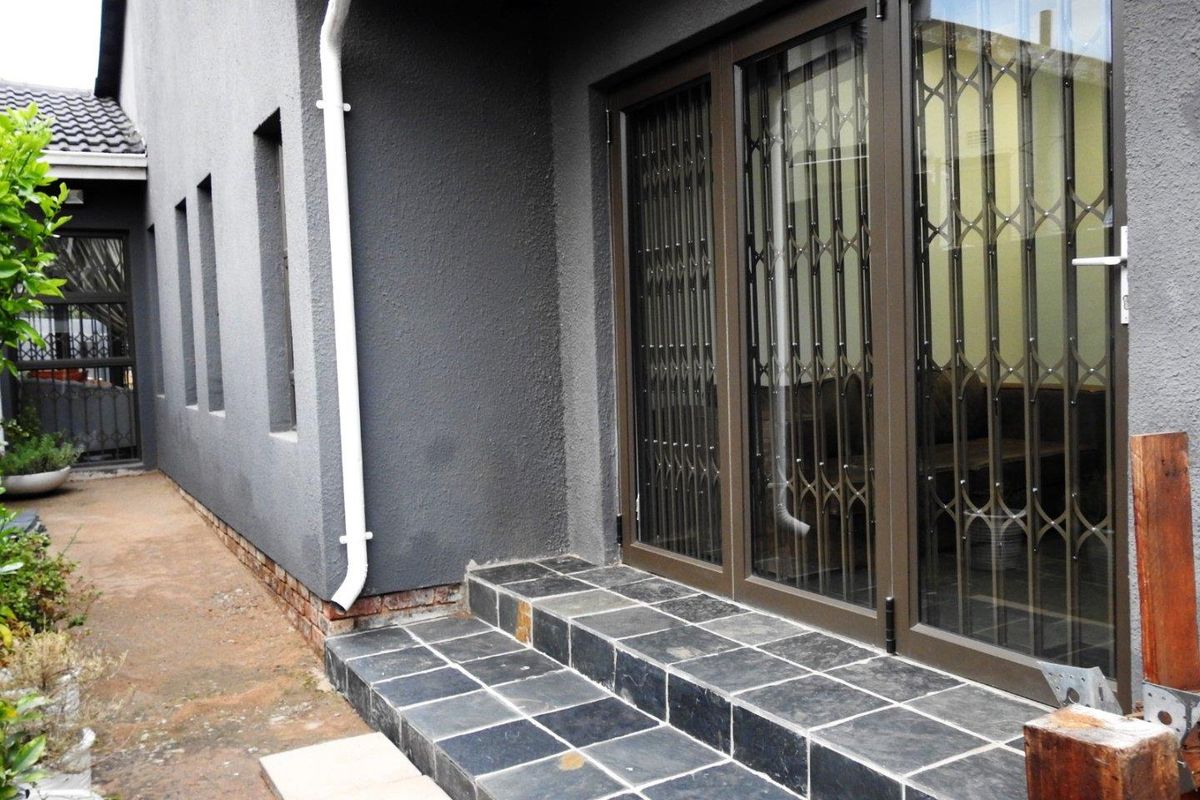 Rear exterior view featuring slate tiled steps leading to aluminium sliding doors with security gates and a textured dark grey wall finish.