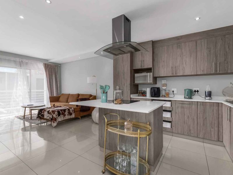 Modern open-plan living area featuring a contemporary kitchen with an island, sleek cabinetry, and direct access to a balcony through sliding glass doors.