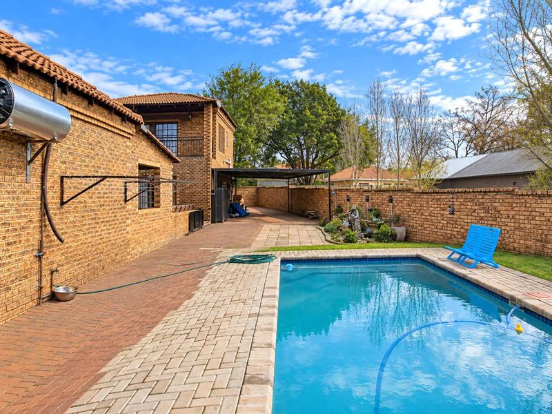 Outdoor pool area featuring a paved patio, brick boundary walls, and a solar water heater mounted on the exterior brick facade.