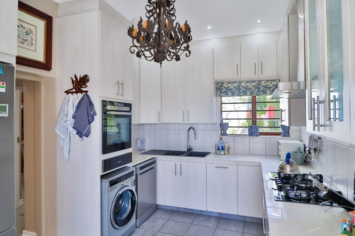 A functional kitchen featuring white cabinetry, integrated oven, gas hob, extractor fan, and built-in laundry appliance space with tiled flooring.