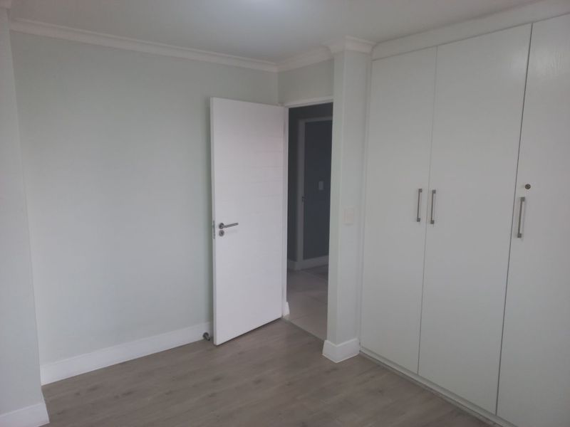 A clean, empty bedroom featuring light-toned laminate flooring, neutral walls, and ample built-in cupboard storage.