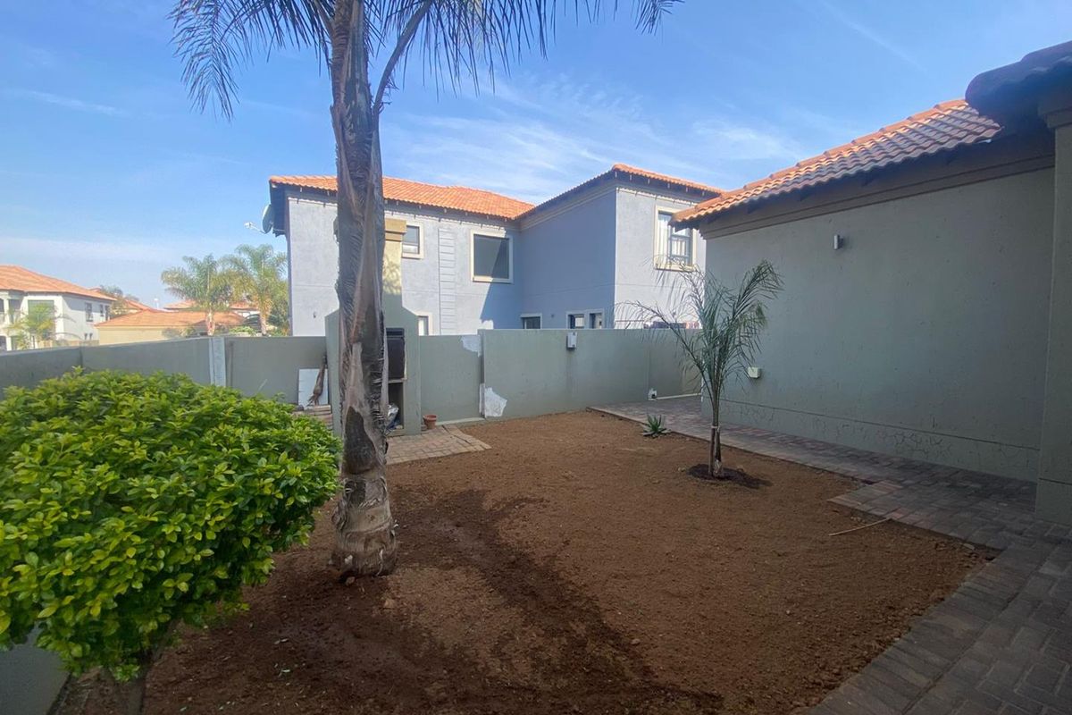 Rear garden area featuring a built-in braai, paved pathways, and boundary walls, currently requiring landscaping and finishing touches.