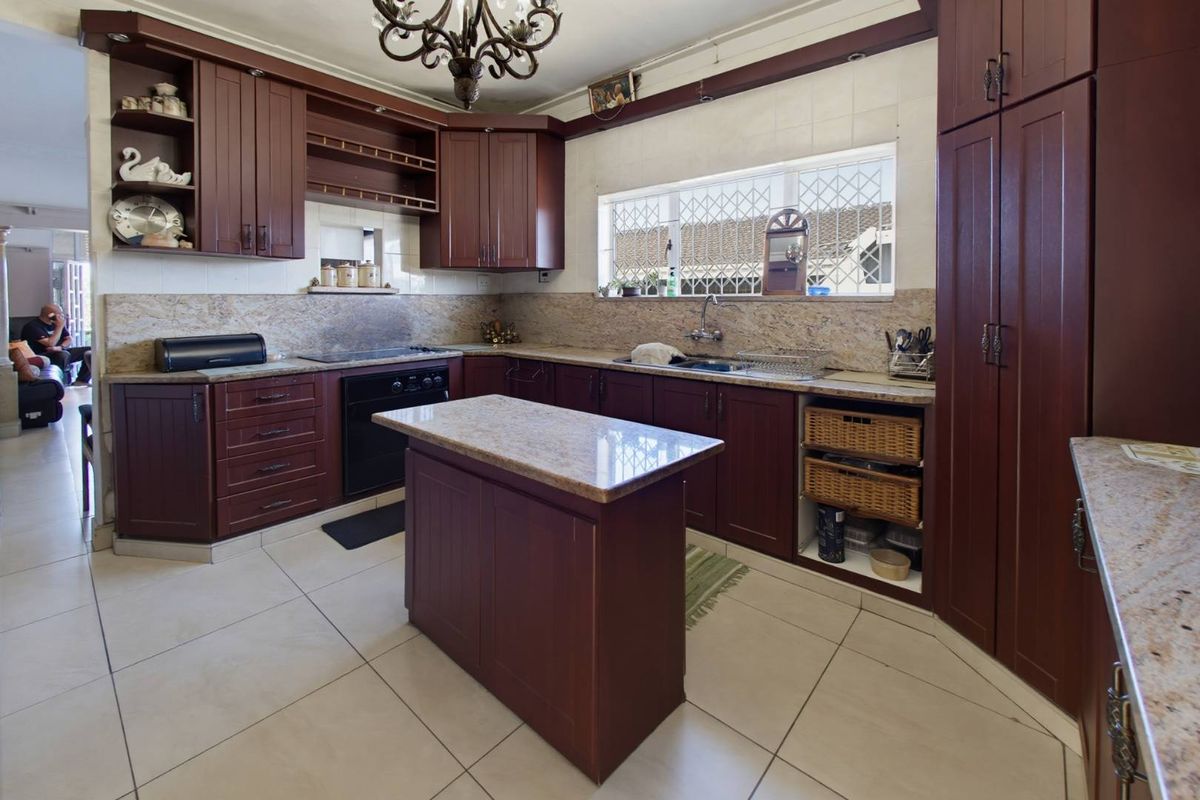 A functional kitchen featuring dark wood cabinetry, granite countertops, a central island, and tiled flooring, offering ample storage and workspace.