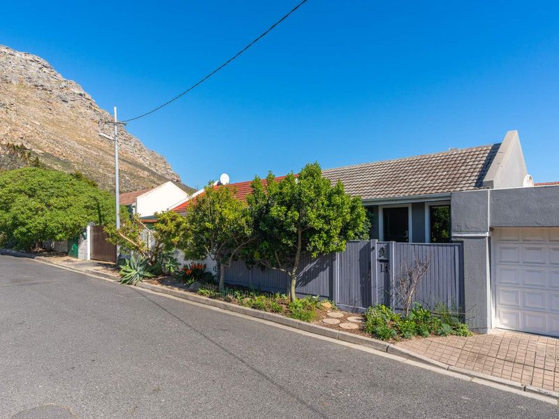 Street view of the property featuring a tiled roof, grey boundary fencing, and a private garage entrance with mountain backdrop.