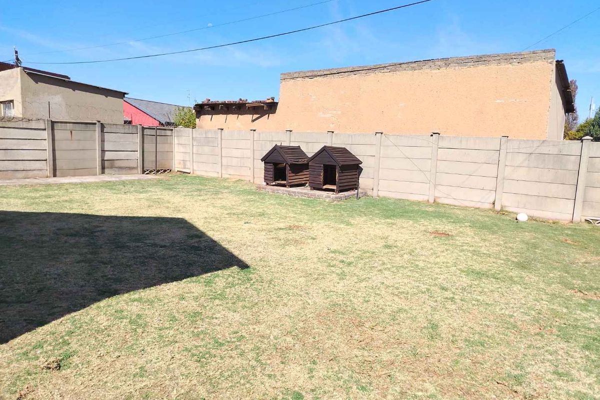 A spacious rear garden area featuring a large lawn enclosed by a precast concrete boundary wall.
