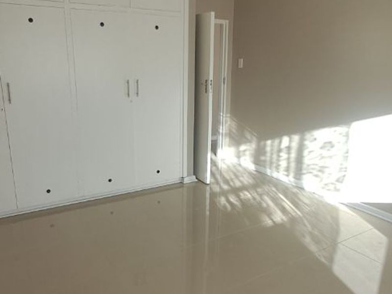 A bright, empty bedroom featuring neutral tiled flooring and extensive white built-in cupboards, offering a clean and versatile living space.
