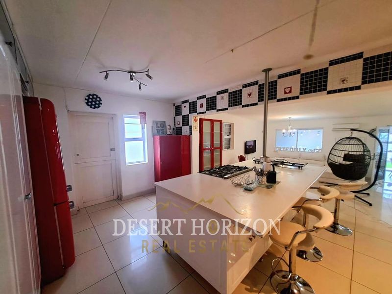 Open plan kitchen and living area featuring a central island with gas hob, tiled flooring, and decorative wall tiling.