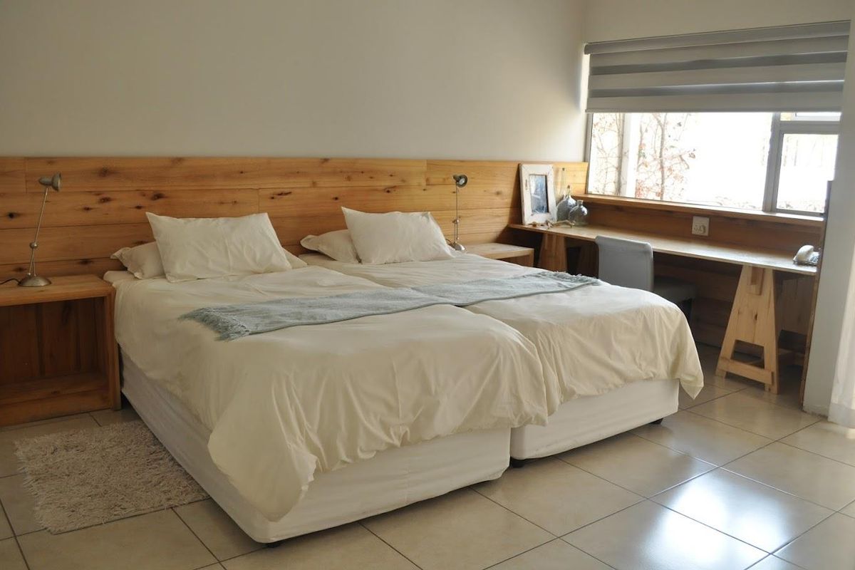 A well-maintained bedroom featuring a built-in wooden headboard, integrated desk space, tiled flooring, and a large window with roller blinds.