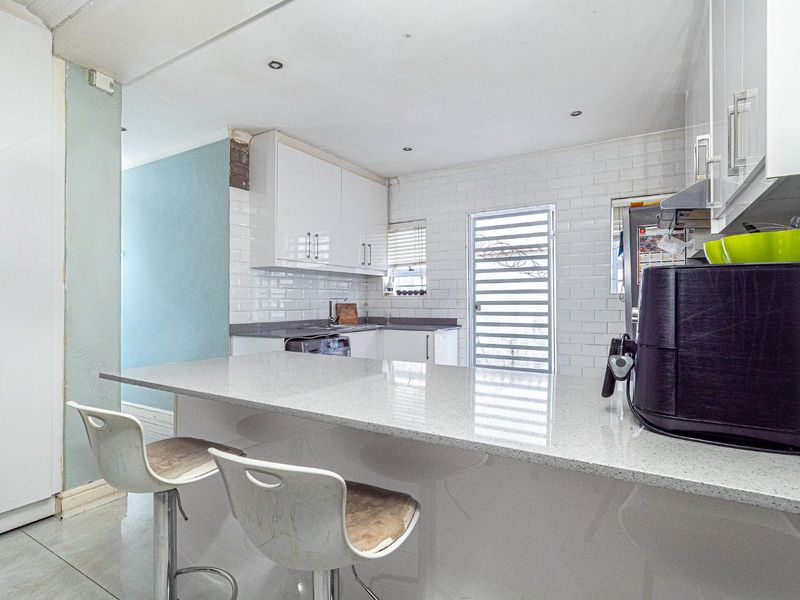 Modern kitchen featuring white cabinetry, quartz countertops, a breakfast bar, and subway tile backsplash with direct access to the exterior.