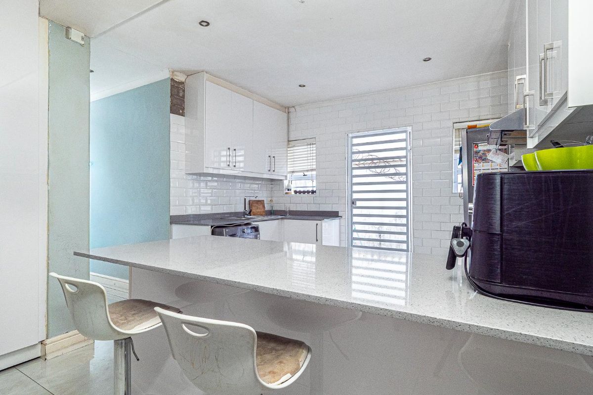 Modern kitchen featuring white cabinetry, quartz countertops, a breakfast bar, and subway tile backsplash with direct access to the exterior.