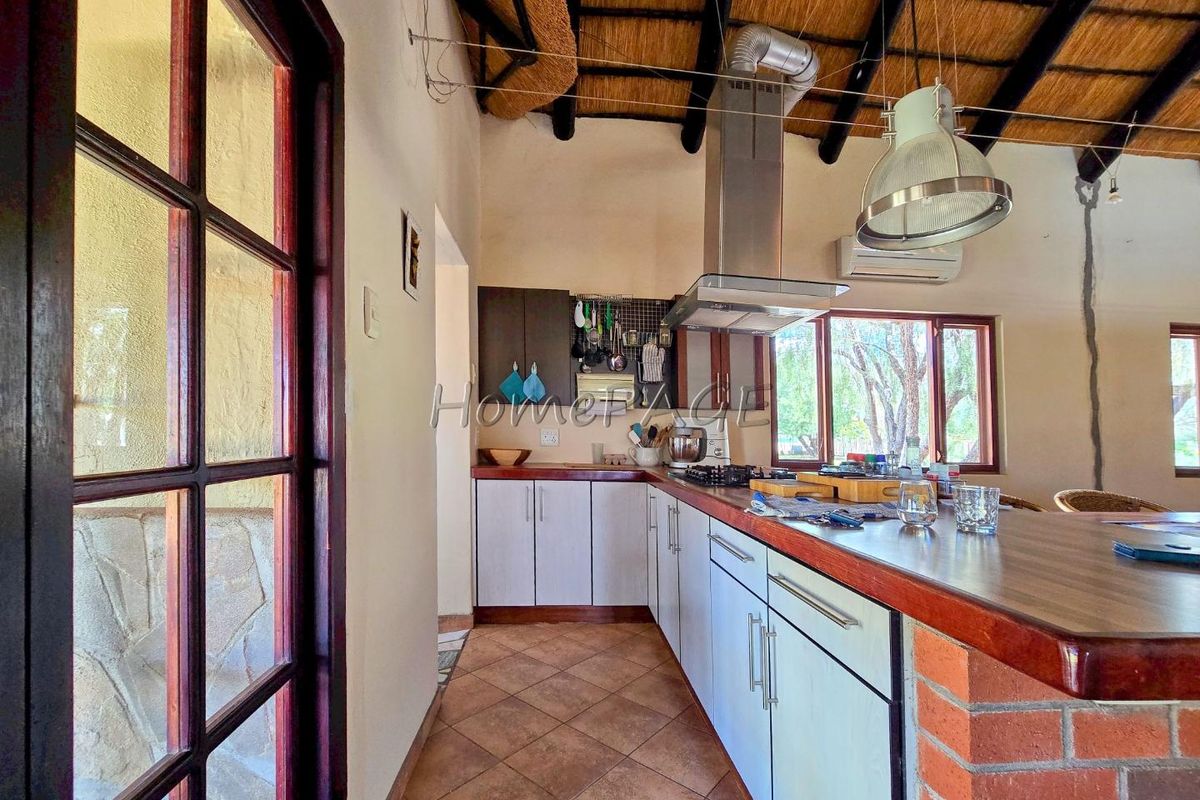 A rustic kitchen featuring a thatched roof, wooden cabinetry, a breakfast bar with brick base, and a stainless steel extractor fan.