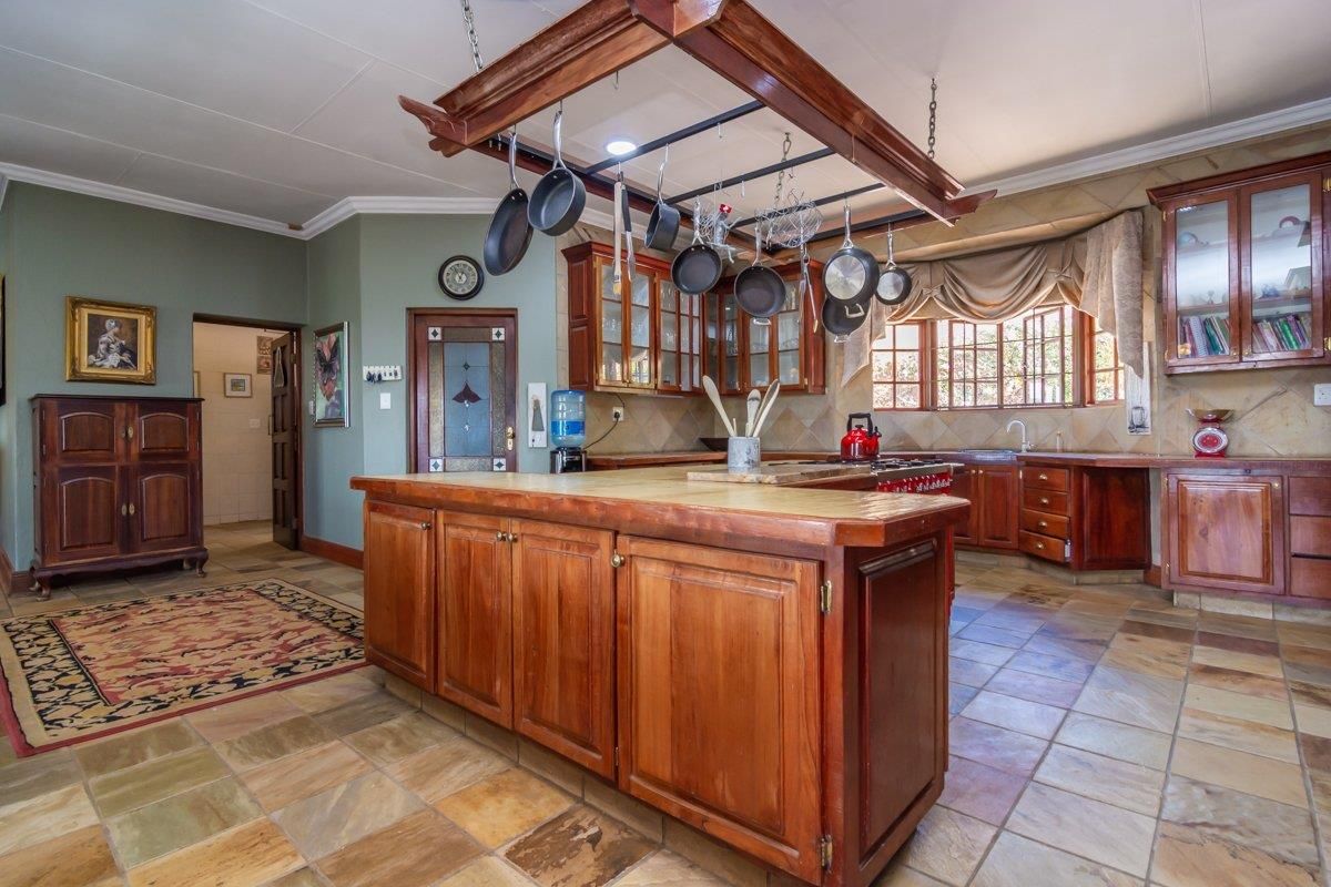 Spacious kitchen featuring solid wood cabinetry, a central island with a wooden countertop, a hanging pot rack, and natural stone tile flooring.