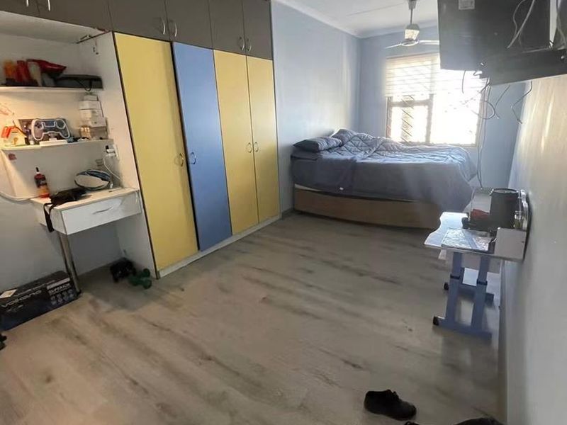 A bedroom featuring laminate flooring, a ceiling fan, and extensive built-in cupboard storage with a integrated desk area.