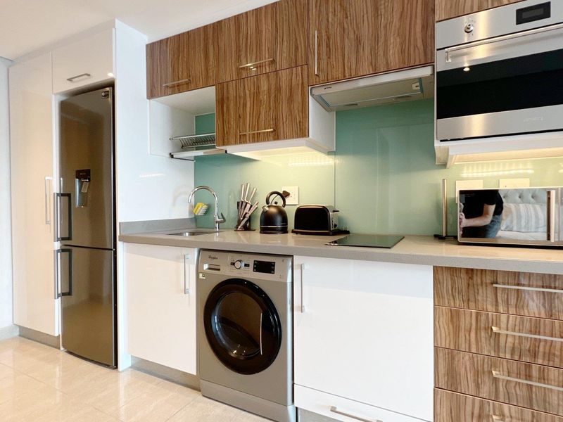 Modern kitchen featuring sleek two-tone cabinetry, stone countertops, glass splashback, and integrated appliances including an oven, microwave, and hob.