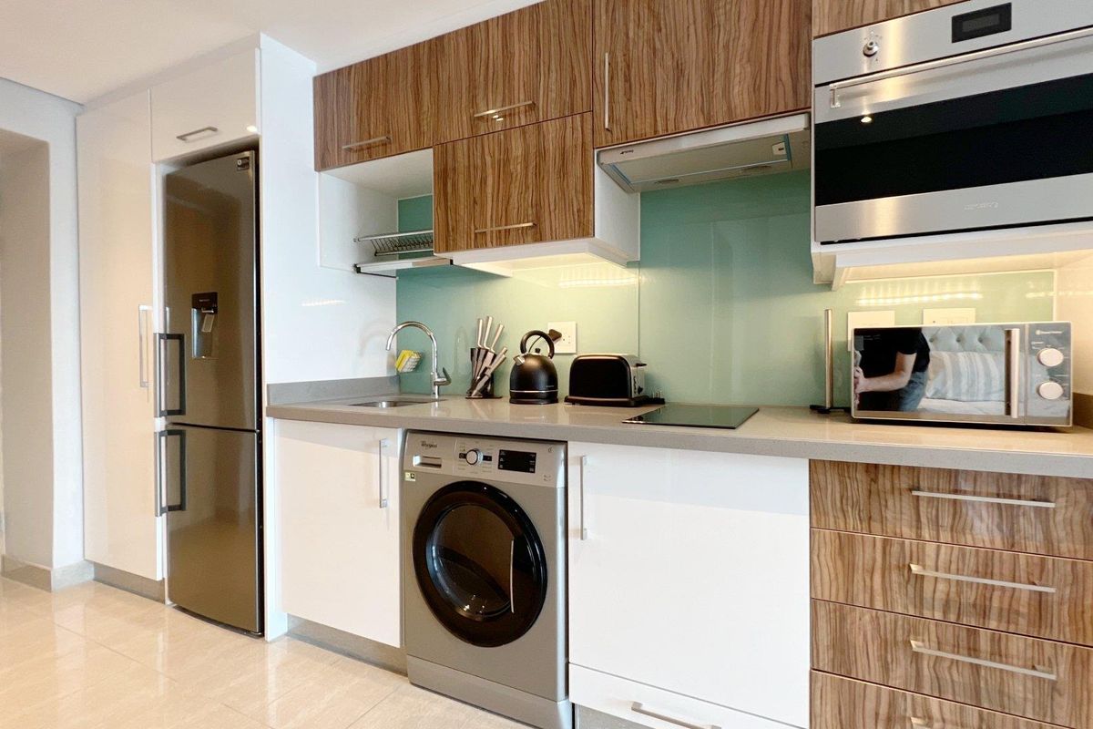 Modern kitchen featuring sleek two-tone cabinetry, stone countertops, glass splashback, and integrated appliances including an oven, microwave, and hob.