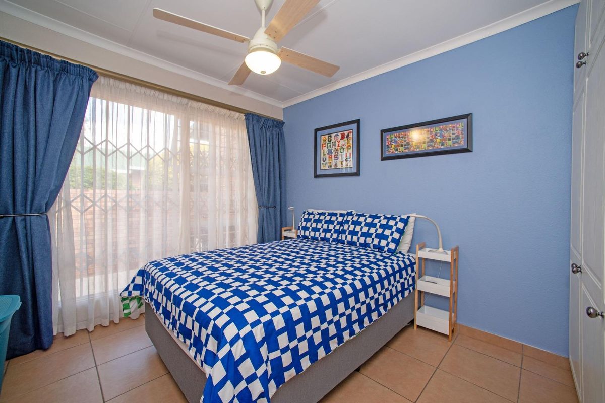 A well-maintained bedroom featuring tiled flooring, a ceiling fan, and built-in cupboards, with direct access to the exterior via a sliding door.