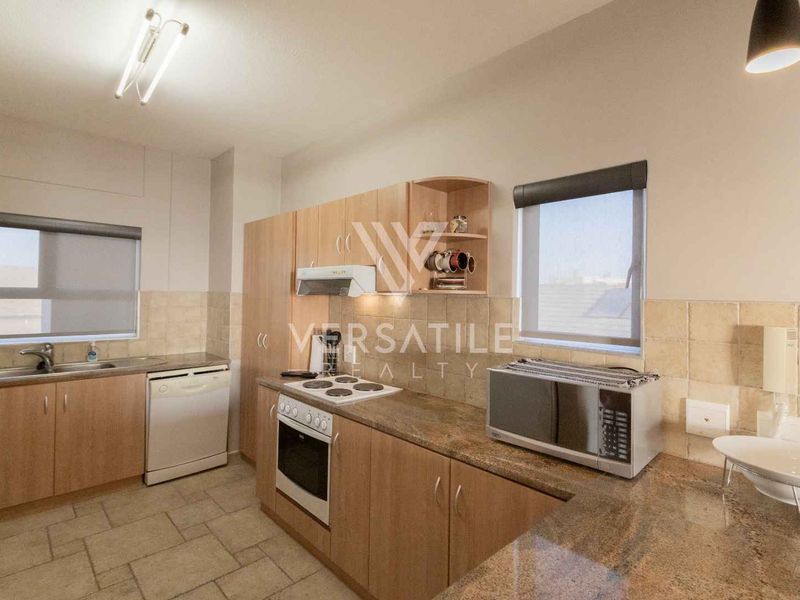 A functional kitchen featuring laminate cabinetry, granite countertops, built-in oven with hob, extractor fan, and tiled finishes throughout.