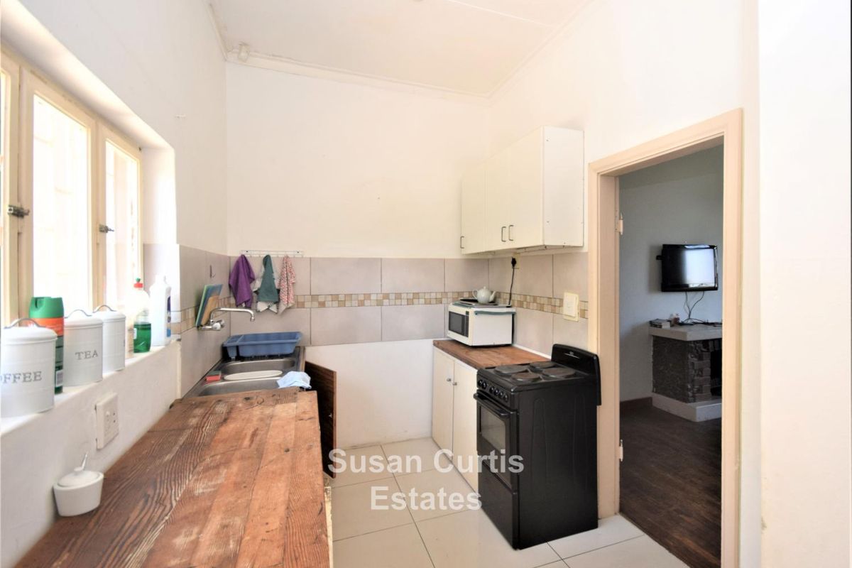 A compact kitchen featuring tiled flooring, a double sink, built-in cabinetry, and a freestanding stove, with direct access to an adjacent living area.
