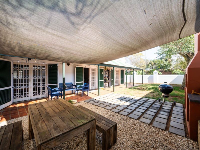 Covered outdoor patio area featuring a built-in braai, shade sail, and direct access to the garden through multiple security-gated doors.