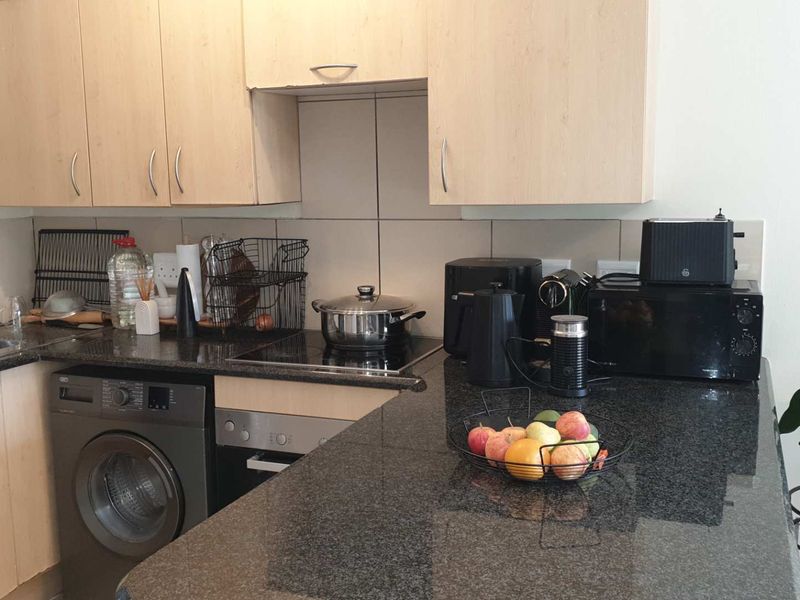A functional kitchen featuring granite countertops, light wood-finish cabinetry, a tiled backsplash, and integrated appliances including an oven, hob, and washing machine.