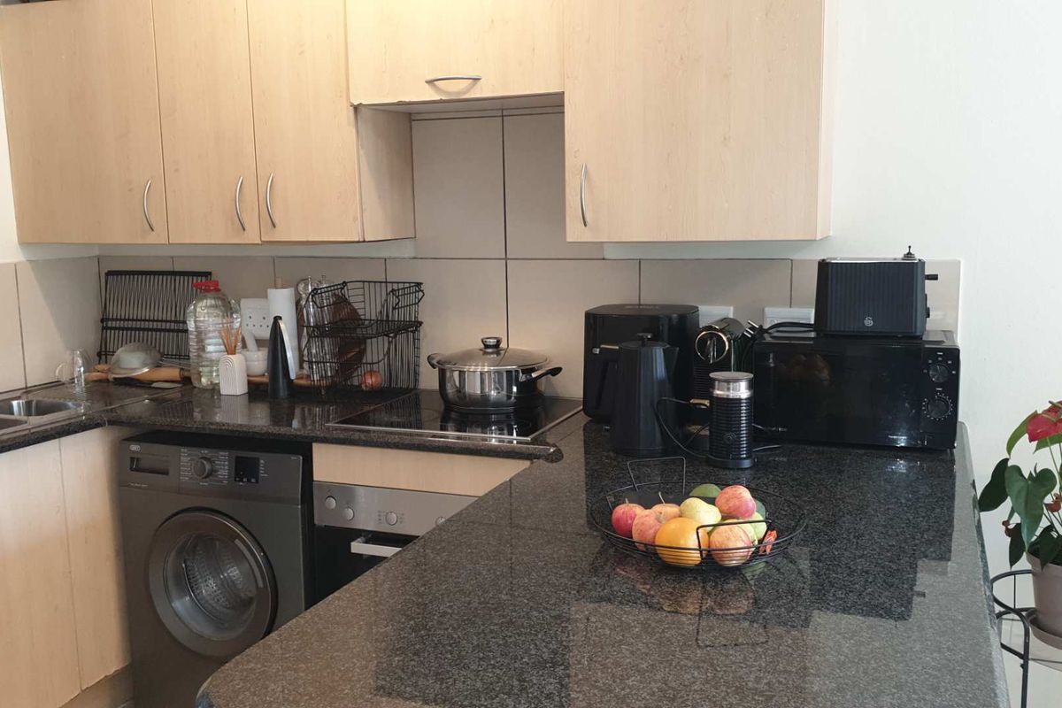 A functional kitchen featuring granite countertops, light wood-finish cabinetry, a tiled backsplash, and integrated appliances including an oven, hob, and washing machine.