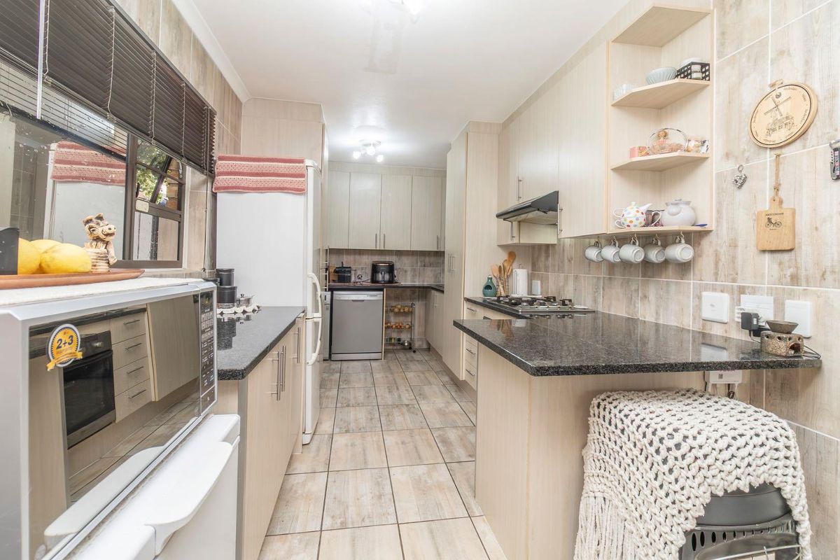A functional kitchen featuring granite countertops, light wood cabinetry, tiled flooring, a built-in gas hob, and an extractor fan.