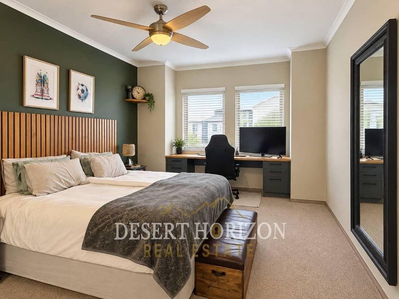 A well-maintained bedroom featuring a built-in desk, ceiling fan, and neutral carpeting, offering a functional space with a modern accent wall.