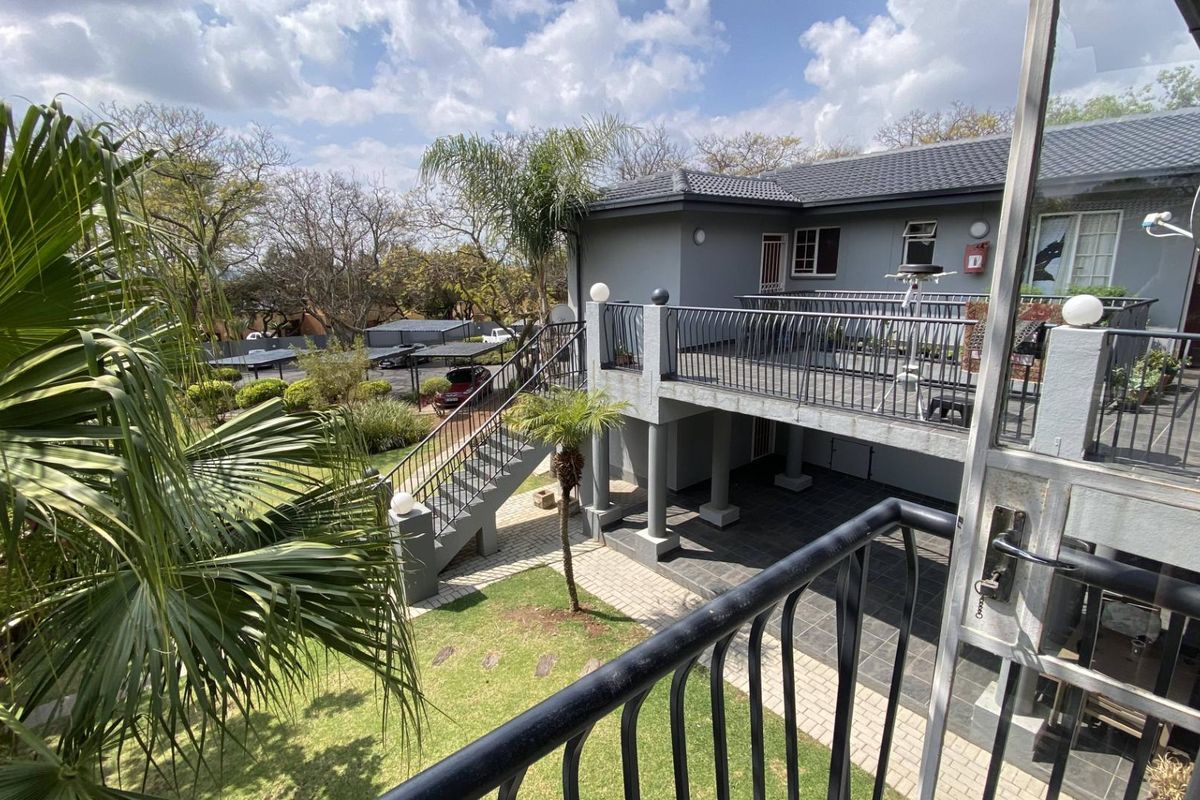 View of the rear exterior featuring a raised balcony with metal railings, an external staircase, and a paved patio area overlooking the garden.