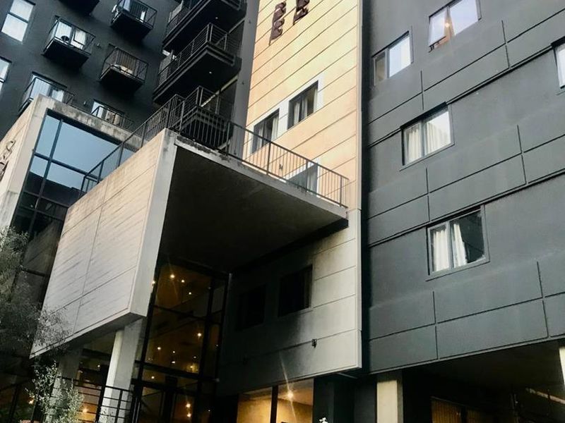 Modern multi-story apartment building facade featuring dark cladding, prominent balconies, and a stone-stepped entrance.