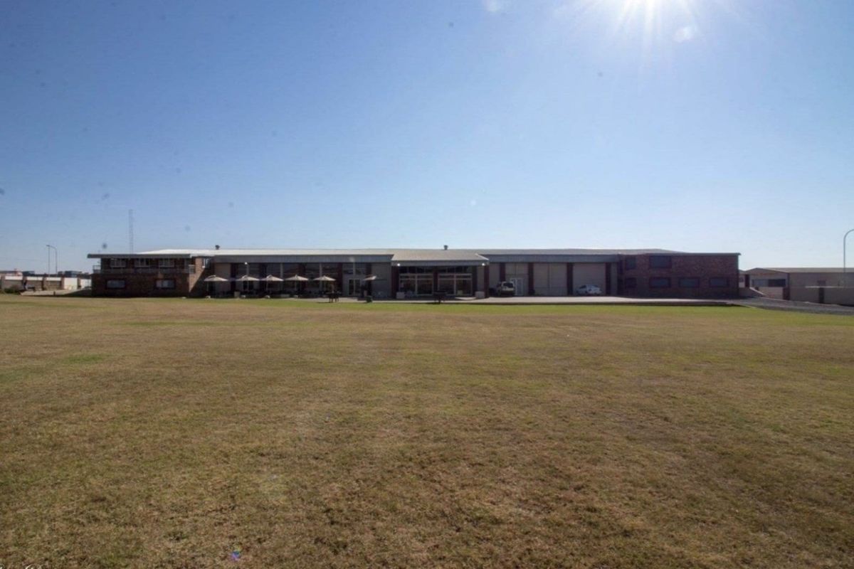 Wide-angle view of the rear commercial property facade featuring a large open lawn, paved parking area, and covered outdoor space.