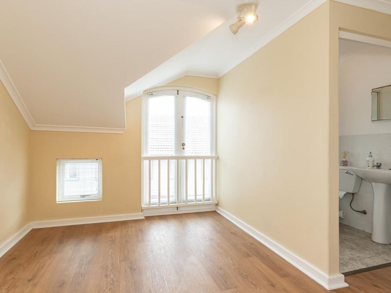 An empty bedroom featuring laminate flooring, coved ceilings, and french doors leading to a small balcony, with an adjoining en-suite bathroom.