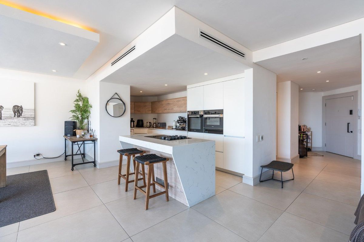Modern open-plan kitchen featuring a stone-topped island, integrated appliances, sleek cabinetry, and recessed ceiling lighting in a contemporary penthouse setting.