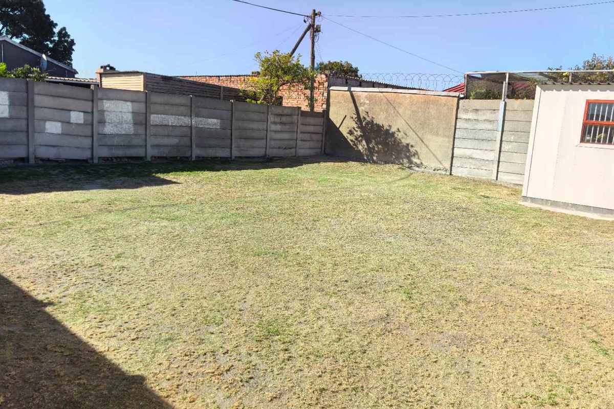 A spacious, open backyard area featuring a large lawn enclosed by concrete boundary walls and a small utility structure.