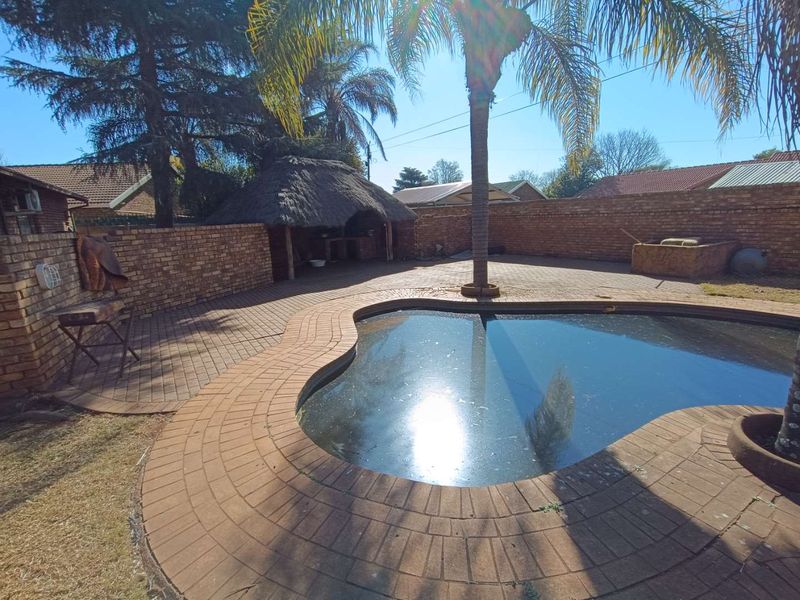 Outdoor pool area featuring a swimming pool, brick paving, and a thatched lapa structure, enclosed by a brick boundary wall.