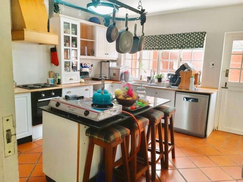 A functional kitchen featuring built-in cabinetry, a central island with granite countertops, integrated appliances, and durable terracotta floor tiles.