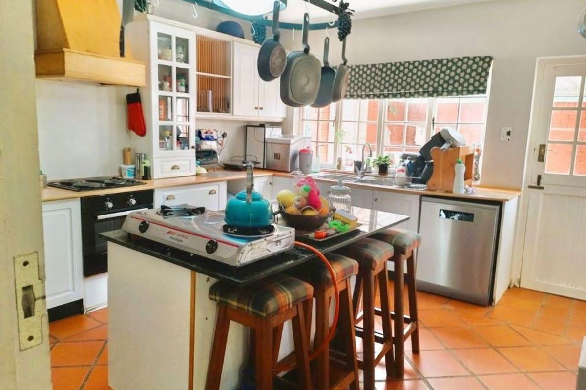 A functional kitchen featuring built-in cabinetry, a central island with granite countertops, integrated appliances, and durable terracotta floor tiles.
