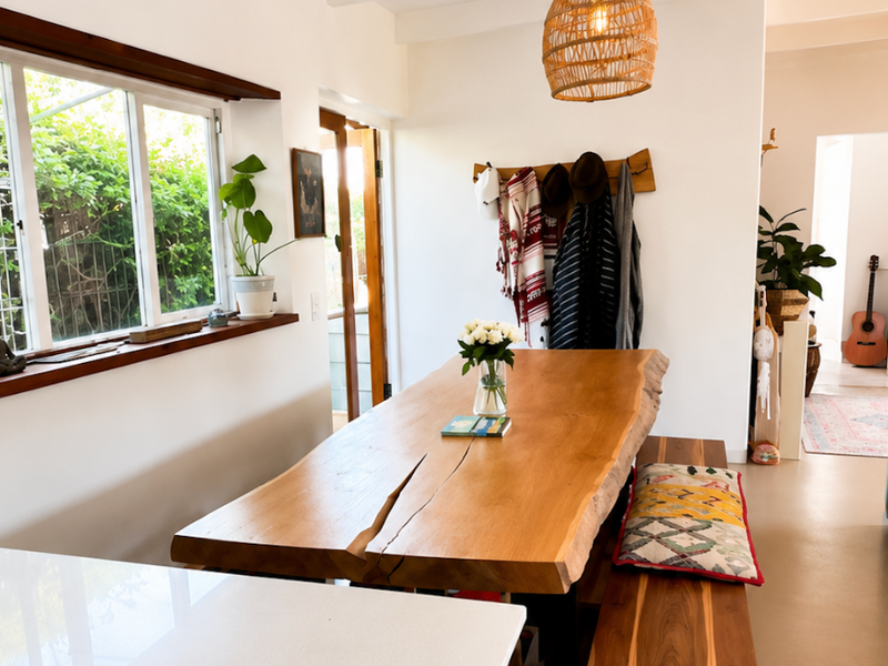 Bright dining area featuring exposed ceiling beams, natural timber window frames, and a modern stone-topped kitchen peninsula.