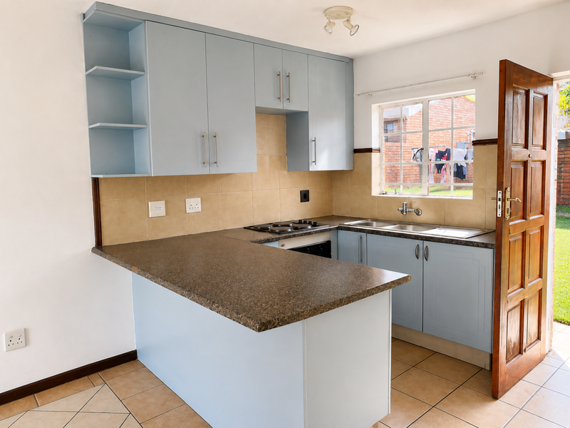 A functional kitchen featuring light blue cabinetry, laminate countertops, a built-in hob and oven, and tiled flooring with direct access to the exterior.