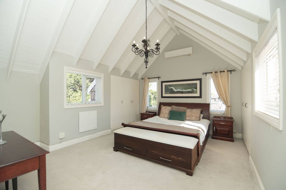 Spacious bedroom featuring a high vaulted ceiling with exposed beams, built-in cabinetry, and a wall-mounted air conditioning unit.