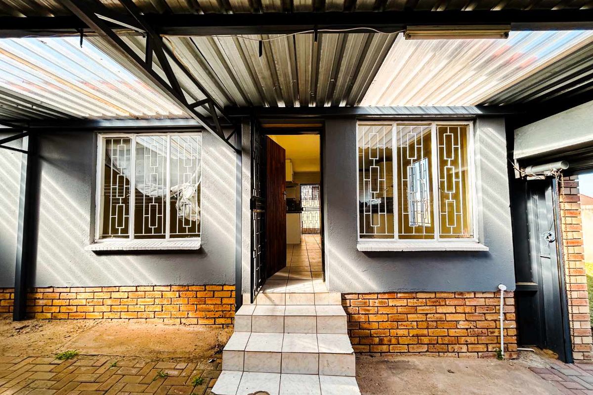 Covered patio area featuring a corrugated metal roof, brick base detailing, and tiled steps leading to the main entrance.