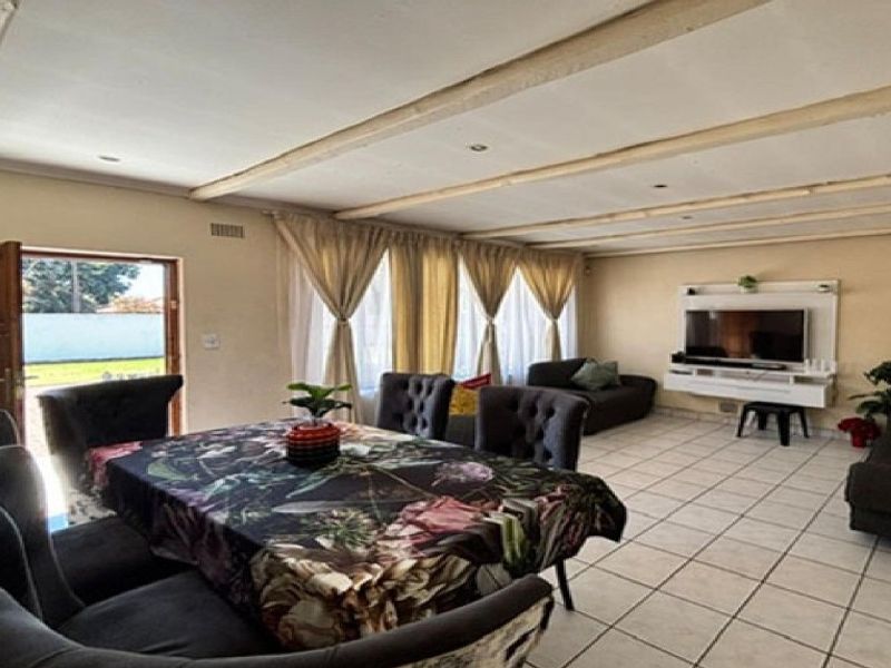 Spacious open-plan living and dining area featuring tiled flooring, exposed ceiling beams, and a built-in media unit with direct access to the garden.