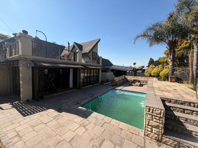 Outdoor pool area featuring a stone-paved patio, built-in stone retaining walls, and a balcony overlooking the swimming pool with folding glass door access.