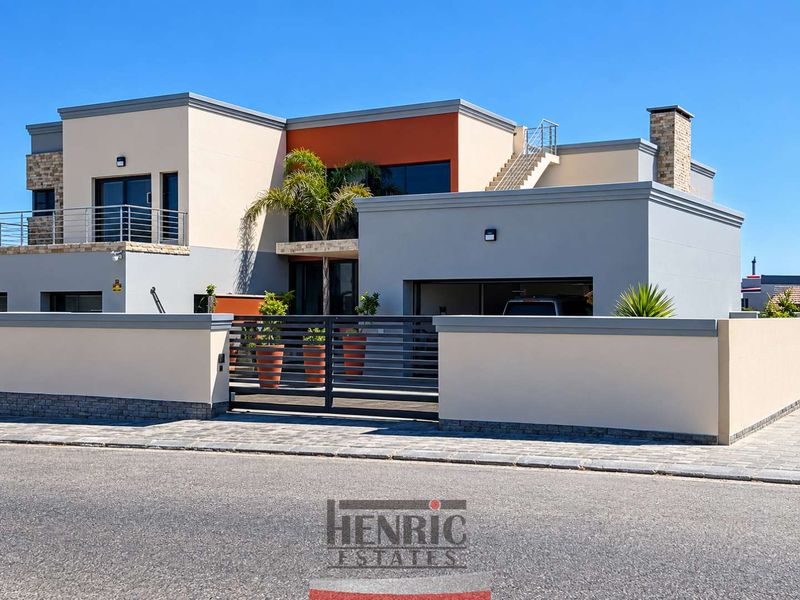 Modern double-story residence featuring clean architectural lines, stone cladding accents, a secure gated entrance, paved driveway, and an external staircase leading to the upper level.