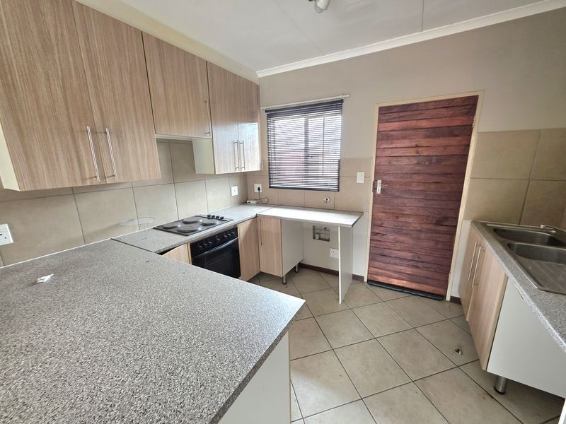 A functional kitchen featuring light wood-look cabinetry, granite-effect laminate countertops, a built-in oven and hob, and tiled flooring throughout.