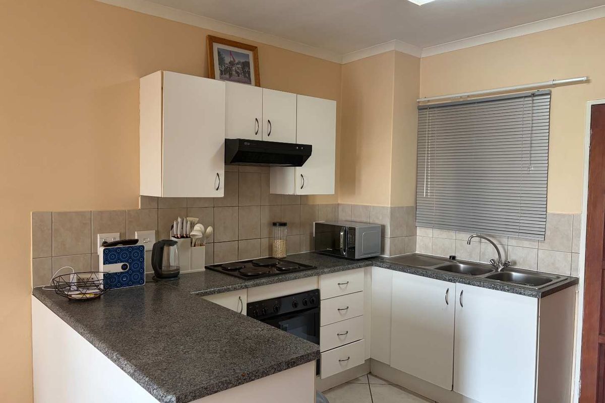 Functional kitchen featuring white cabinetry, granite-look countertops, built-in oven, hob, extractor fan, and a double stainless steel sink with tiled splashback.