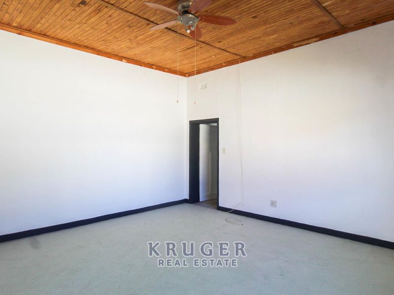 An empty bedroom featuring a timber ceiling with a ceiling fan and neutral wall finishes, ready for renovation or staging.